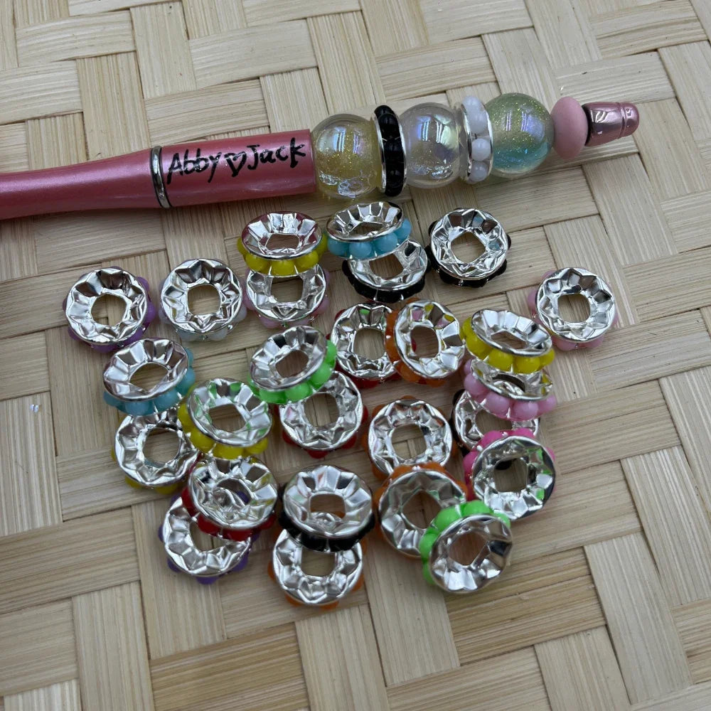 Assorted 15MM faceted silver tone metal spacer beads with colorful side accents shown next to a beadable pen