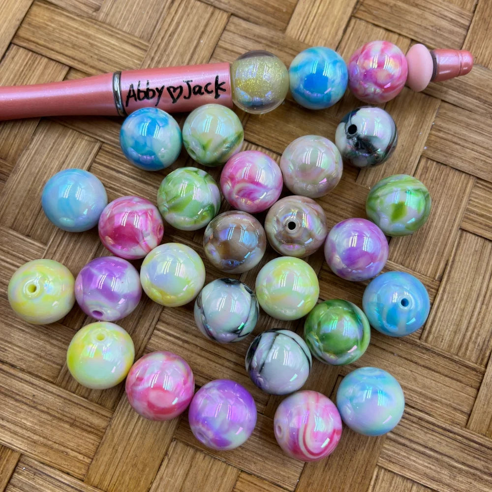 16MM pastel marble swirl AB finish acrylic beads in pink, purple, blue, green, and yellow multicolor patterns displayed on a wicker surface next to a beadable pen.