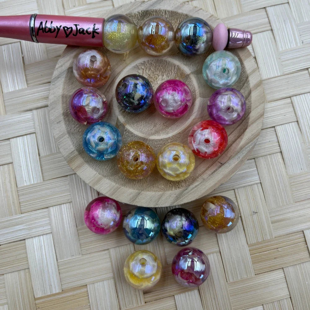 Assorted 16MM round iridescent swirl acrylic beads in pink, blue, gold, purple, red, and teal on a wooden tray beside a beadable pen