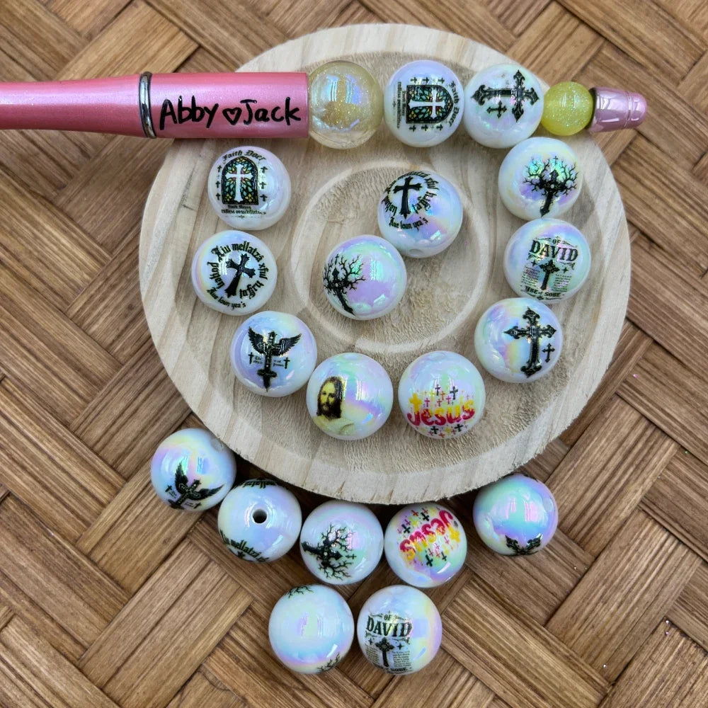16MM iridescent white acrylic beads featuring Christian cross, Jesus face, and religious scripture print designs arranged on a wooden tray with a beadable pen