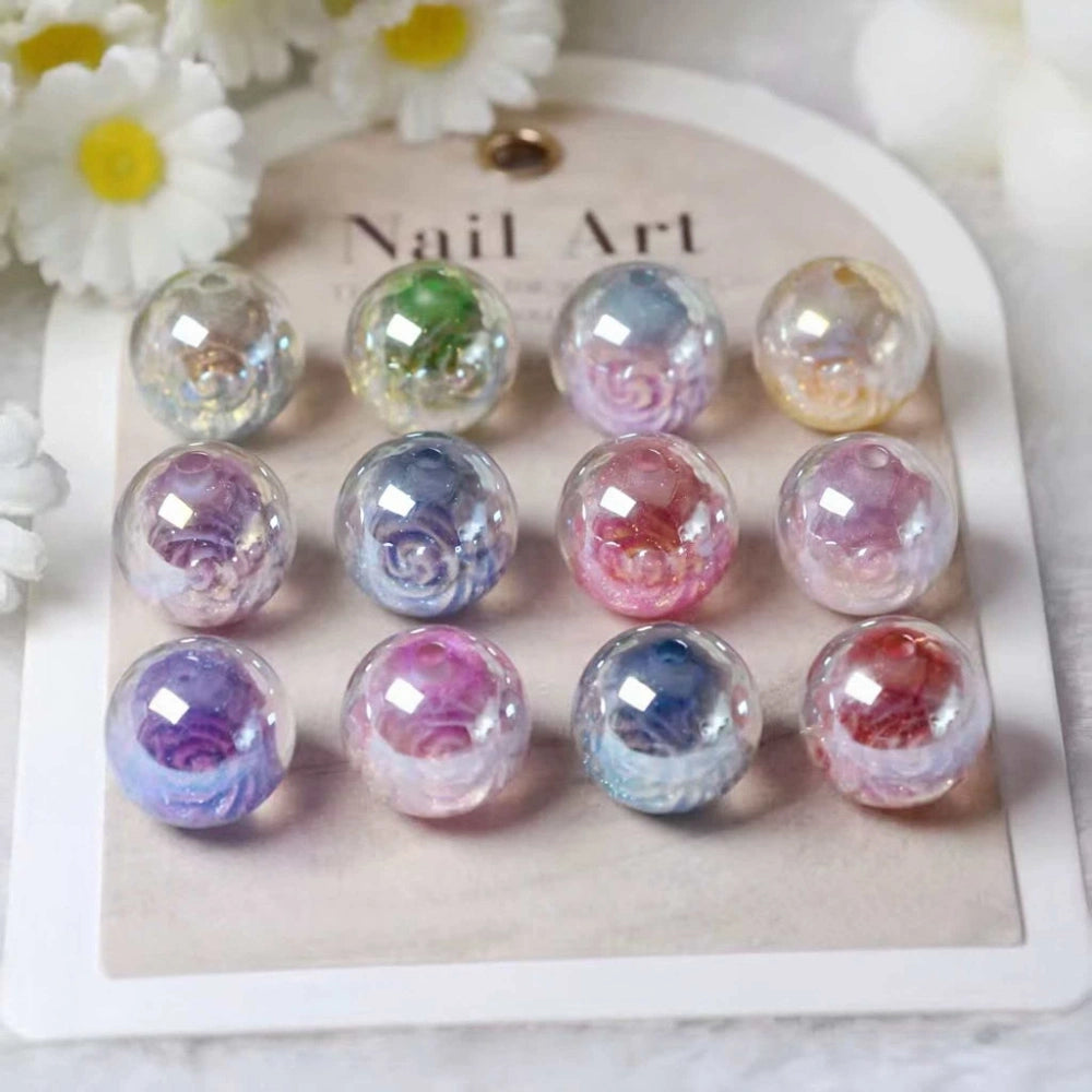 12-piece set of iridescent aurora acrylic round beads with colorful rose swirl designs inside, displayed on a nail art card with white daisy flowers in background.