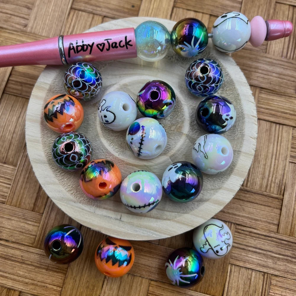 16MM Nightmare Before Christmas acrylic beads featuring Jack Skellington, ghost, pumpkin, and iridescent spider web designs arranged on a wooden disc with a pink beadable pen labeled Abby and Jack.