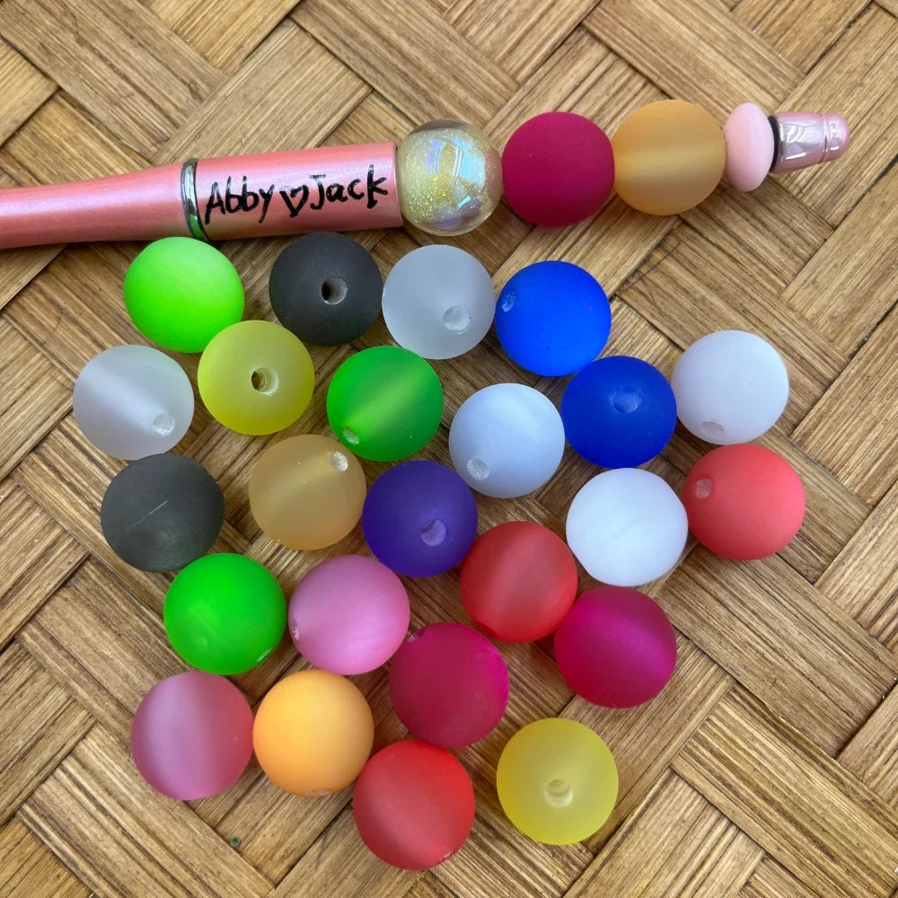 Assorted 16MM frosted round acrylic beads in bright multicolor tones beside a beadable pen.