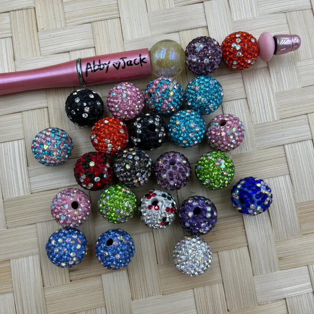 Assorted 16MM round clay rhinestone beads in multicolor sparkle finishes beside a pink beadable pen.