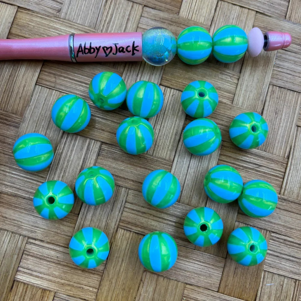 16MM blue and green striped round acrylic beads displayed on a woven surface next to a pink beadable pen, showing vibrant two-tone stripe pattern with center holes.