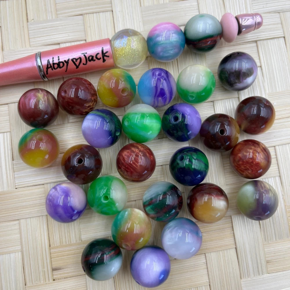 16MM bowling ball swirl multicolor acrylic beads in assorted marbled color combinations displayed on a woven bamboo surface next to a beadable pen.