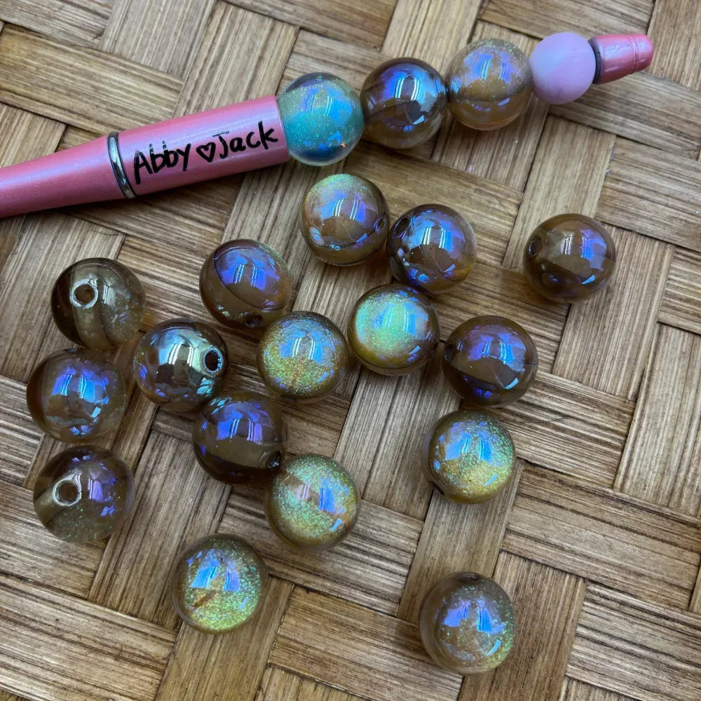 16MM brown aurora iridescent acrylic beads with blue and gold holographic shimmer finish displayed on woven surface next to a pink beadable pen from DIY Mini Planet