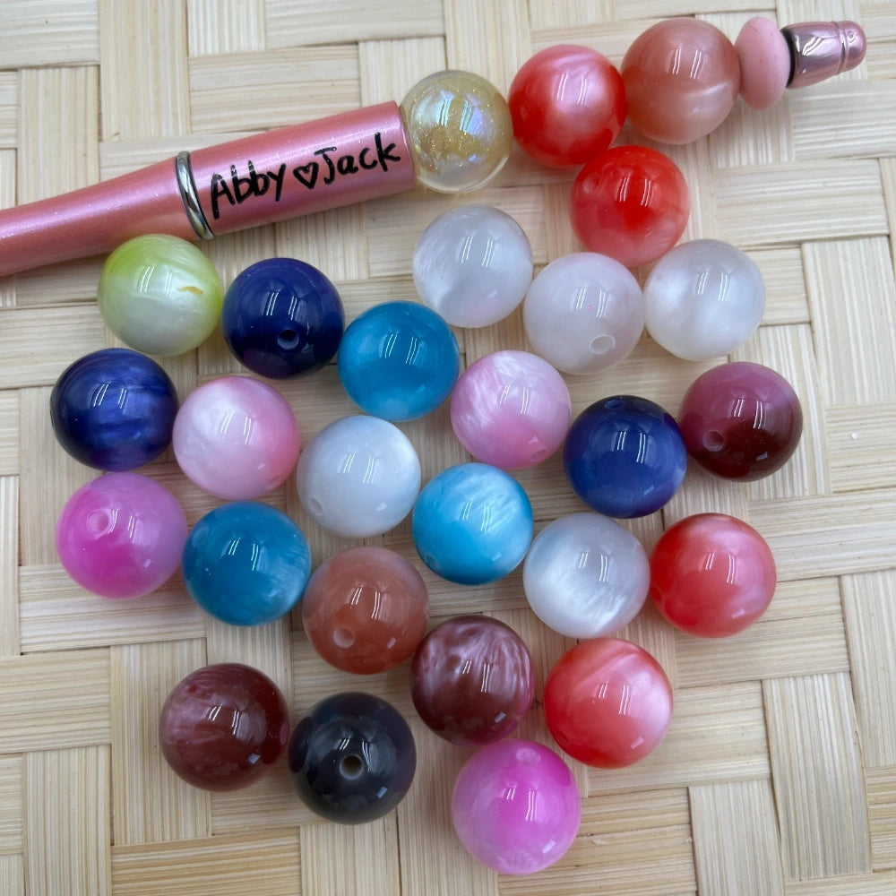 16MM cat eye swirl acrylic beads in assorted colors including pink, red, blue, teal, white, mauve, and black displayed on a woven surface next to a beadable pen.
