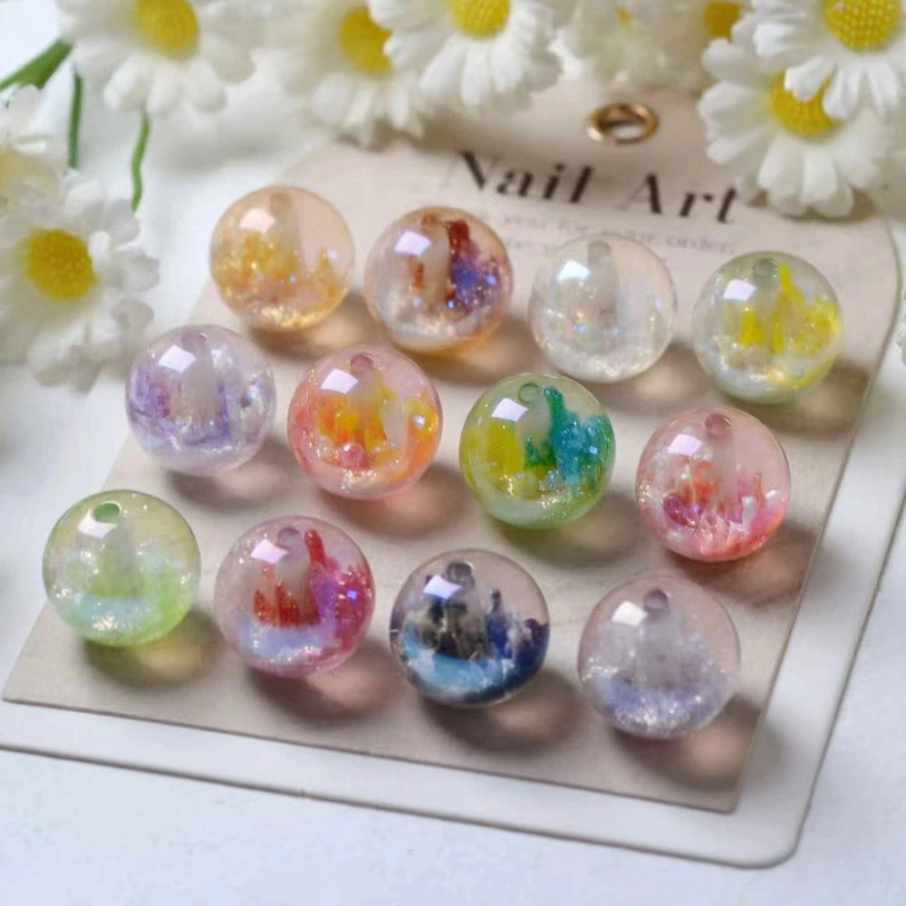 12 assorted 16MM clear acrylic round beads filled with colorful galaxy glitter swirls in pastel pink, purple, green, blue, and yellow, displayed on a nail art card with white daisy flowers in the background.