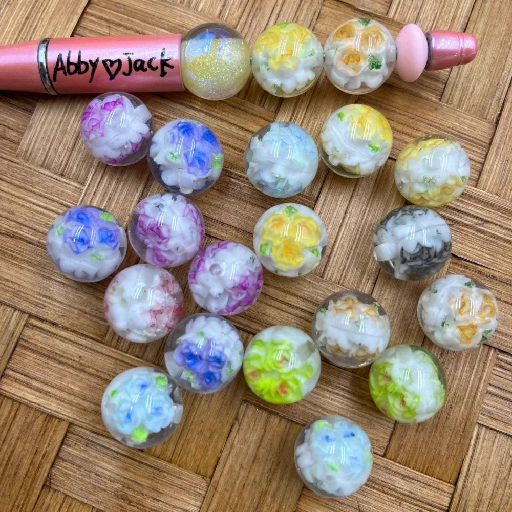 16MM clear acrylic round beads with colorful embedded floral bouquet designs in pink, blue, yellow, purple, and green, displayed on a woven surface next to a beadable pen.