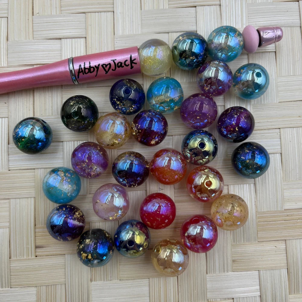 16MM galaxy glitter iridescent acrylic beads with gold foil and multicolor shimmer finish displayed next to a beadable pen on woven surface