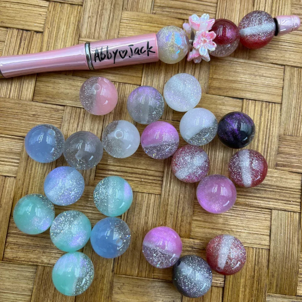 16MM galaxy glitter two-tone acrylic beads in pastel pink, mint, lavender, red, purple, and clear colorways displayed on a woven surface next to a beadable pen.