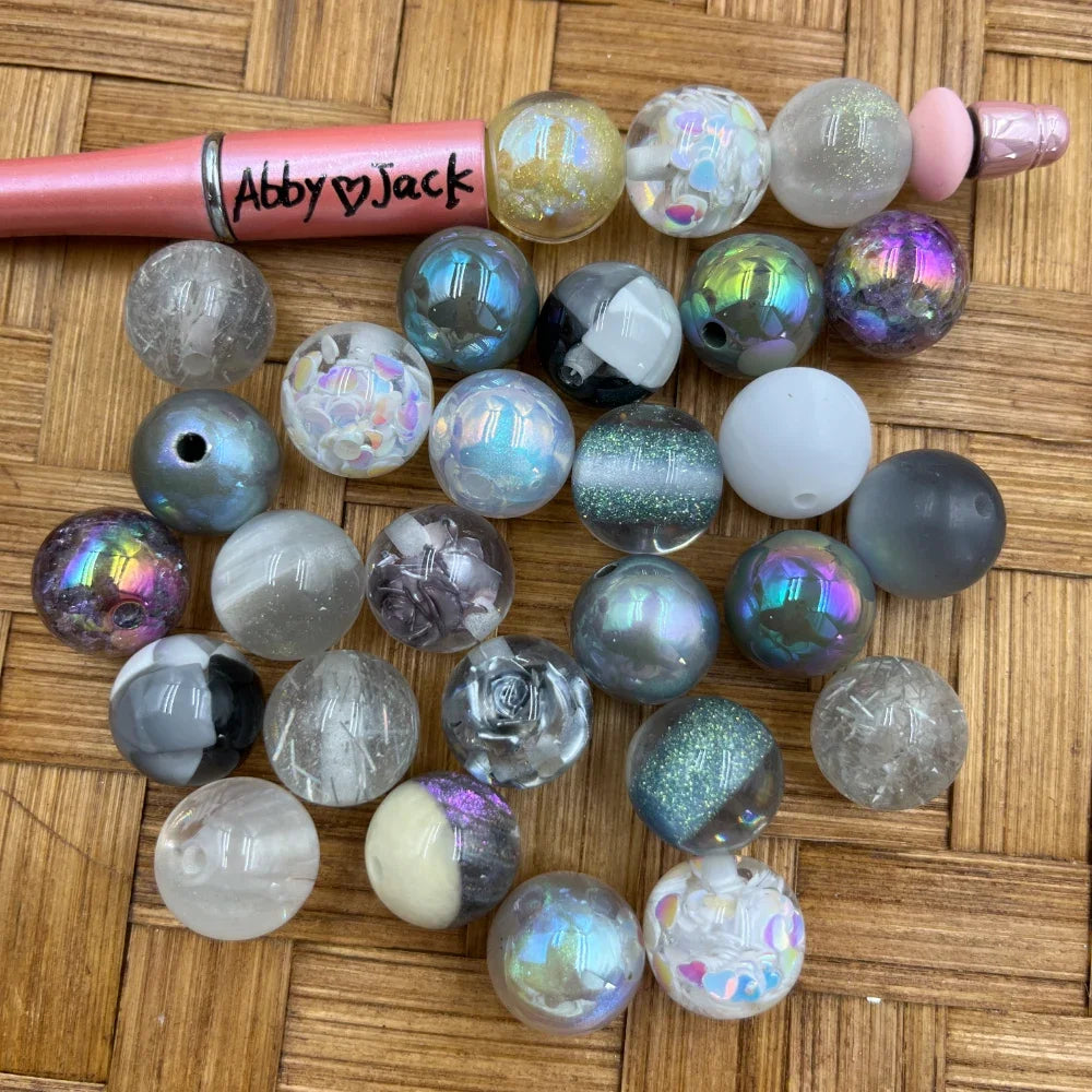 16MM gray iridescent glitter mix acrylic beads assortment including aurora, confetti, rose, crackle, and matte finishes displayed with a pink beadable pen on wicker surface.