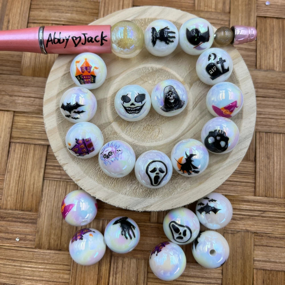 16MM iridescent white acrylic beads with Halloween designs including ghost face, grim reaper, skull, witch, haunted house, bats, and RIP tombstone, displayed on a wooden dish with a beadable pen.