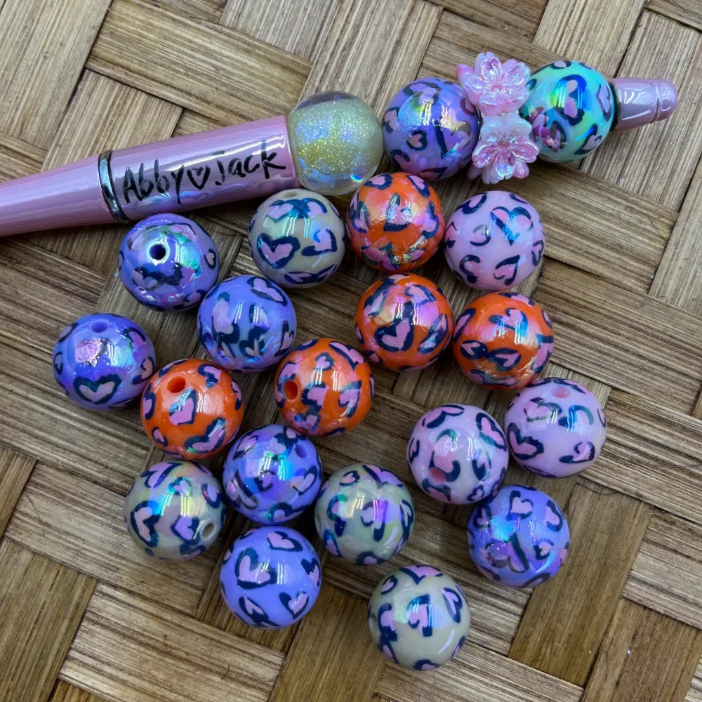 16MM heart leopard print acrylic beads in purple, orange, and pink with iridescent shimmer finish, displayed with a beadable pen on a woven surface