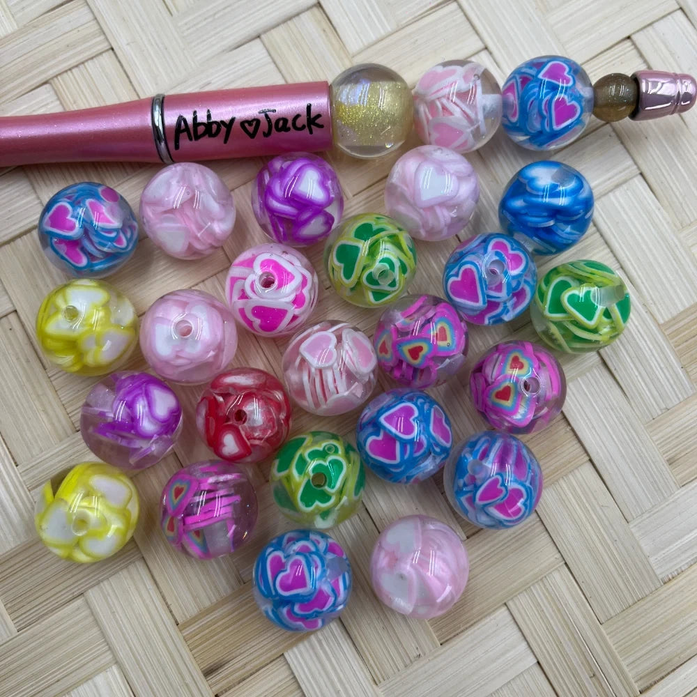 16MM colorful heart print swirl acrylic beads in mixed colors including pink, blue, purple, green and yellow displayed on woven mat next to a beadable pen