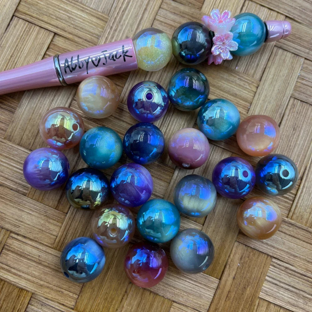16MM iridescent AB aurora acrylic round beads in blue, purple, teal, peach and gold tones displayed on a wicker surface next to a pink beadable pen with flower charm.