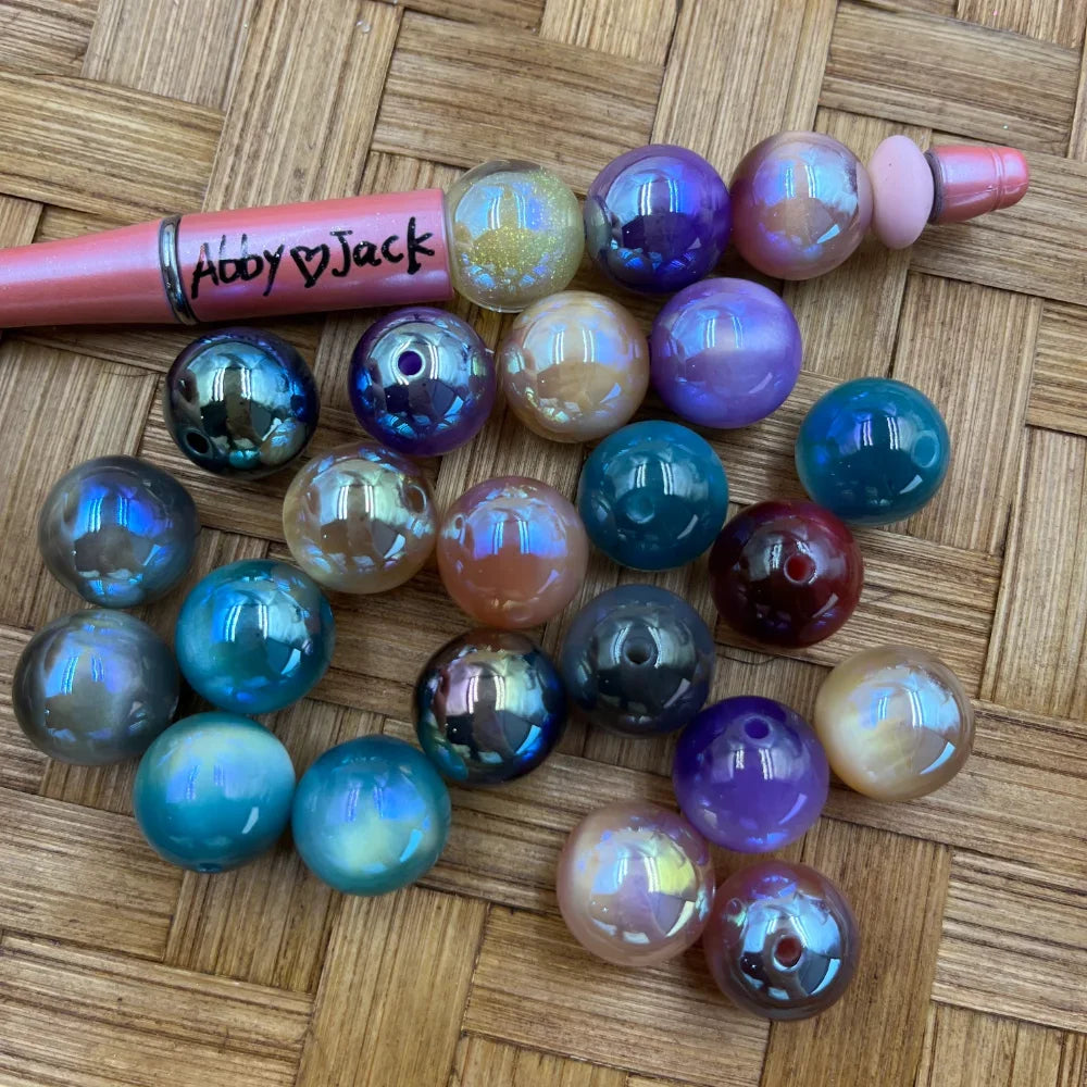16MM iridescent AB finish acrylic beads in assorted colors including teal, purple, blue, silver, burgundy, and champagne displayed on a wicker surface next to a beadable pen.