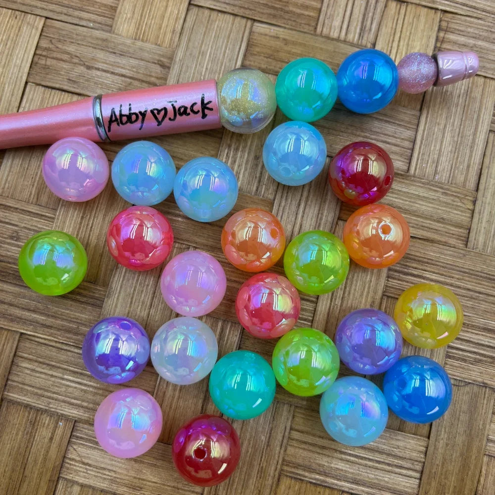 16MM iridescent AB finish round acrylic beads in assorted colors including pink, blue, green, orange, purple, teal, red, and yellow displayed on a woven surface next to a pink beadable pen.
