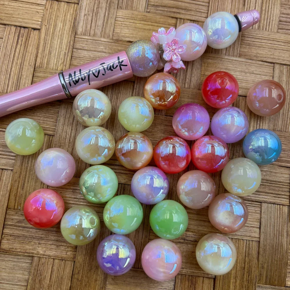 16MM iridescent AB shimmer acrylic beads in assorted pastel and bold colors including pink, green, red, peach, and lilac, displayed on a woven surface next to a beadable pen.
