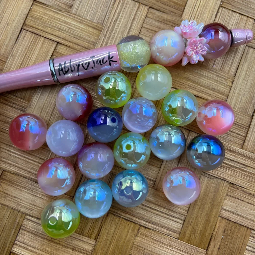 Iridescent aurora glow acrylic beads in pastel pink, blue, green, and red multicolor spread on a wicker surface next to a decorated beadable pen.