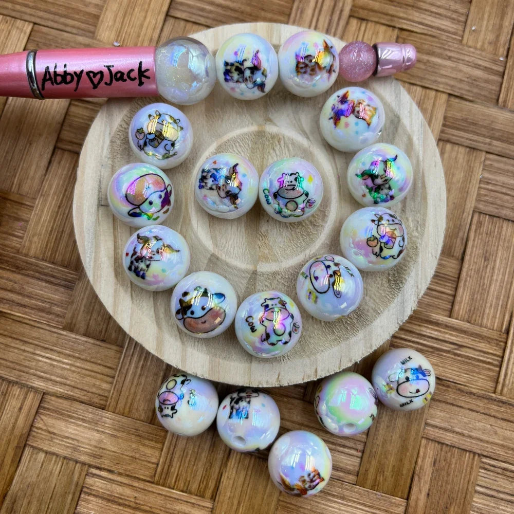 16MM white iridescent acrylic beads featuring colorful cartoon cow designs with aurora shimmer finish, displayed on a wooden tray with a beadable pen