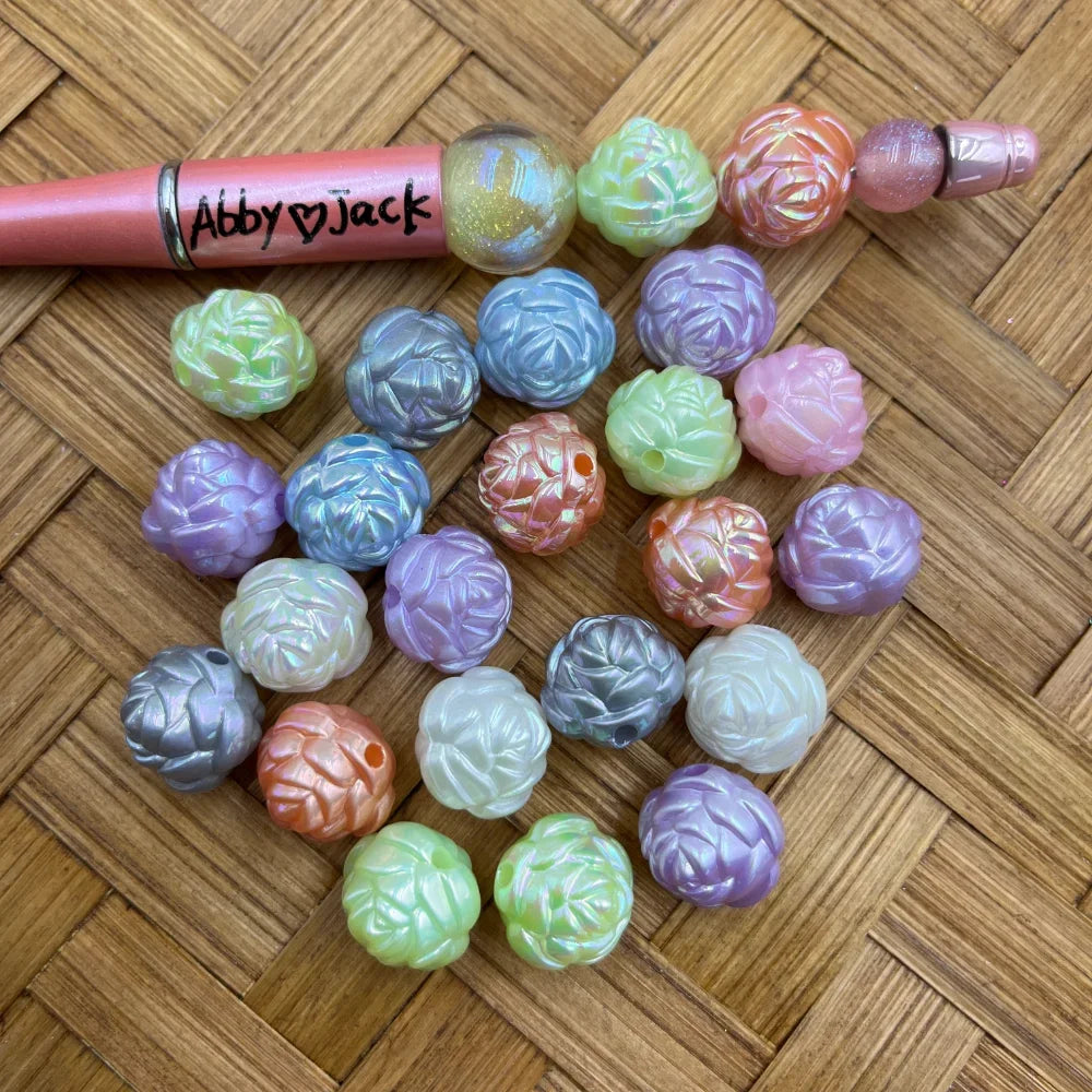 Assorted iridescent pastel rose flower acrylic beads in purple, blue, green, pink, orange, white and silver displayed on a wicker surface next to a beadable pen
