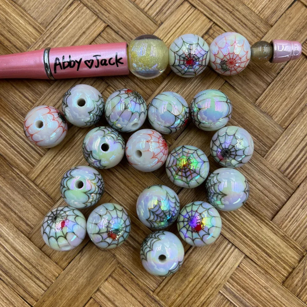 16MM iridescent white acrylic round beads with holographic spiderweb and red spider print design, shown with a beadable pen on a wicker surface