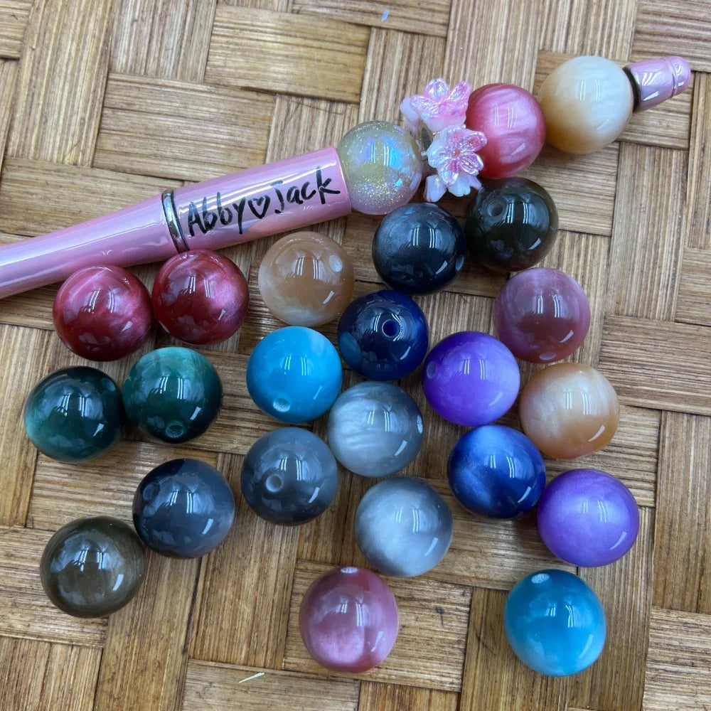 16MM marble swirl acrylic beads in assorted colors including teal, gray, purple, blue, pink, red, and peach displayed on a woven surface next to a beadable pen.
