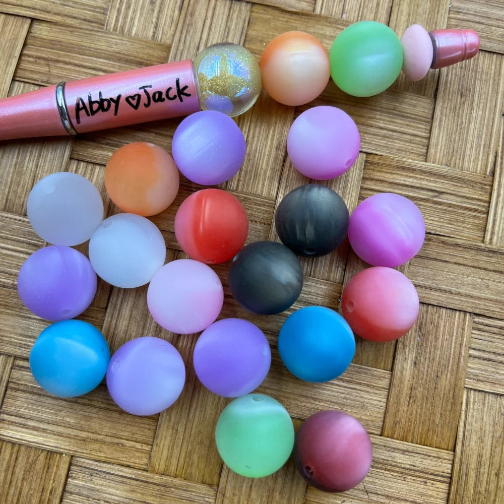 16MM matte pastel mixed color acrylic round beads in purple, blue, pink, green, orange, red, gray, and white displayed on a wicker surface next to a beadable pen.