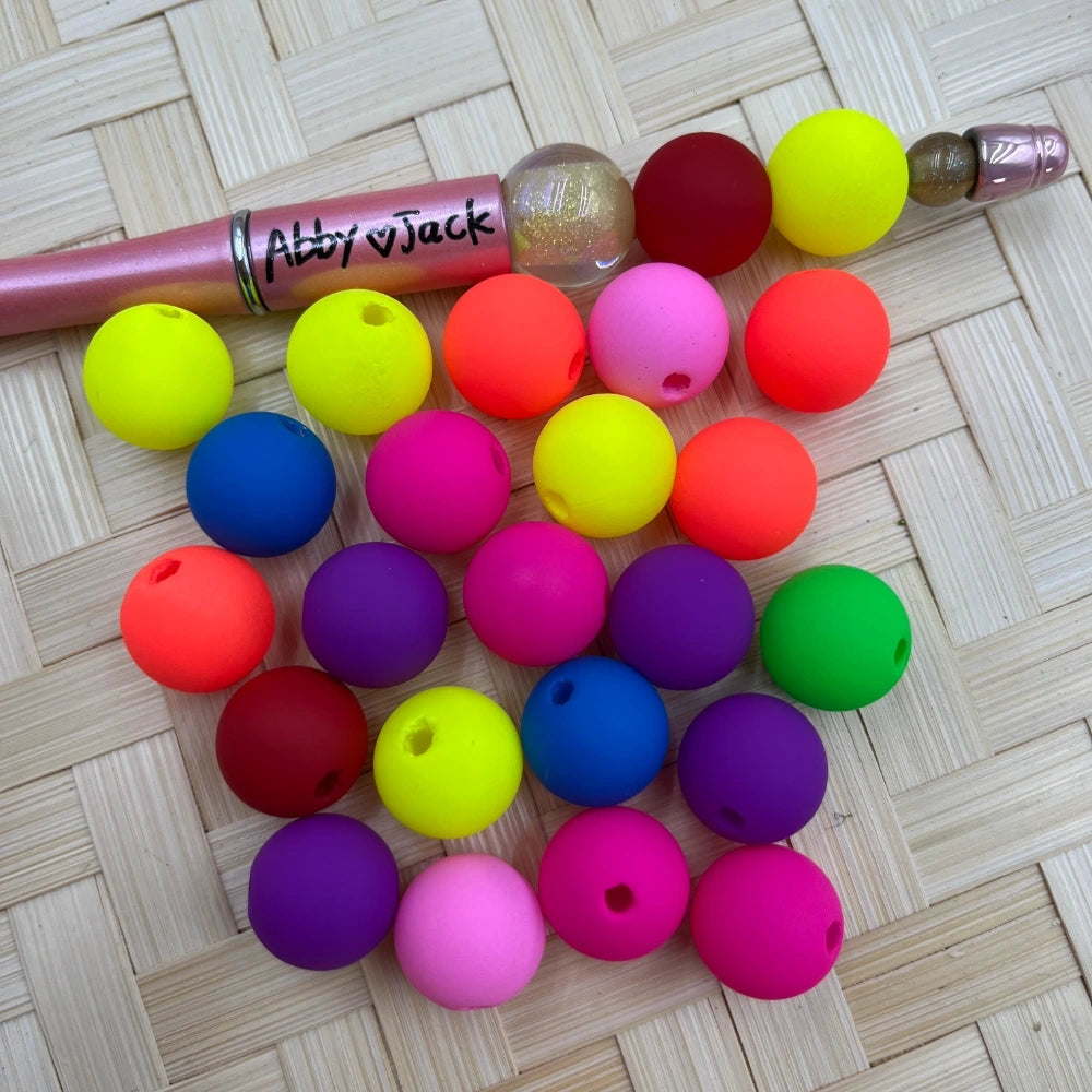 16MM neon matte round acrylic beads in assorted vibrant colors including yellow, orange, pink, purple, red, blue, and green, displayed next to a beadable pen on a wicker surface.