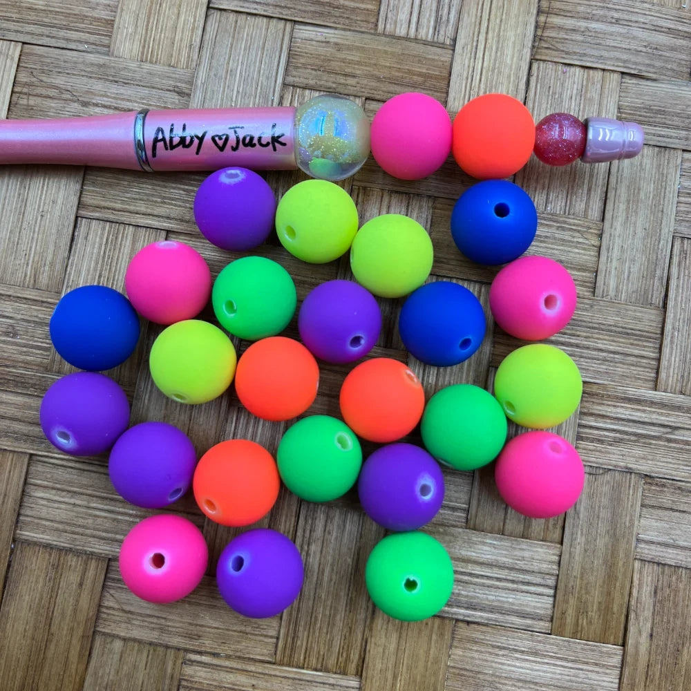 16MM neon matte round acrylic beads in bright neon pink, orange, green, yellow, purple, and blue displayed next to a beadable pen on a woven surface