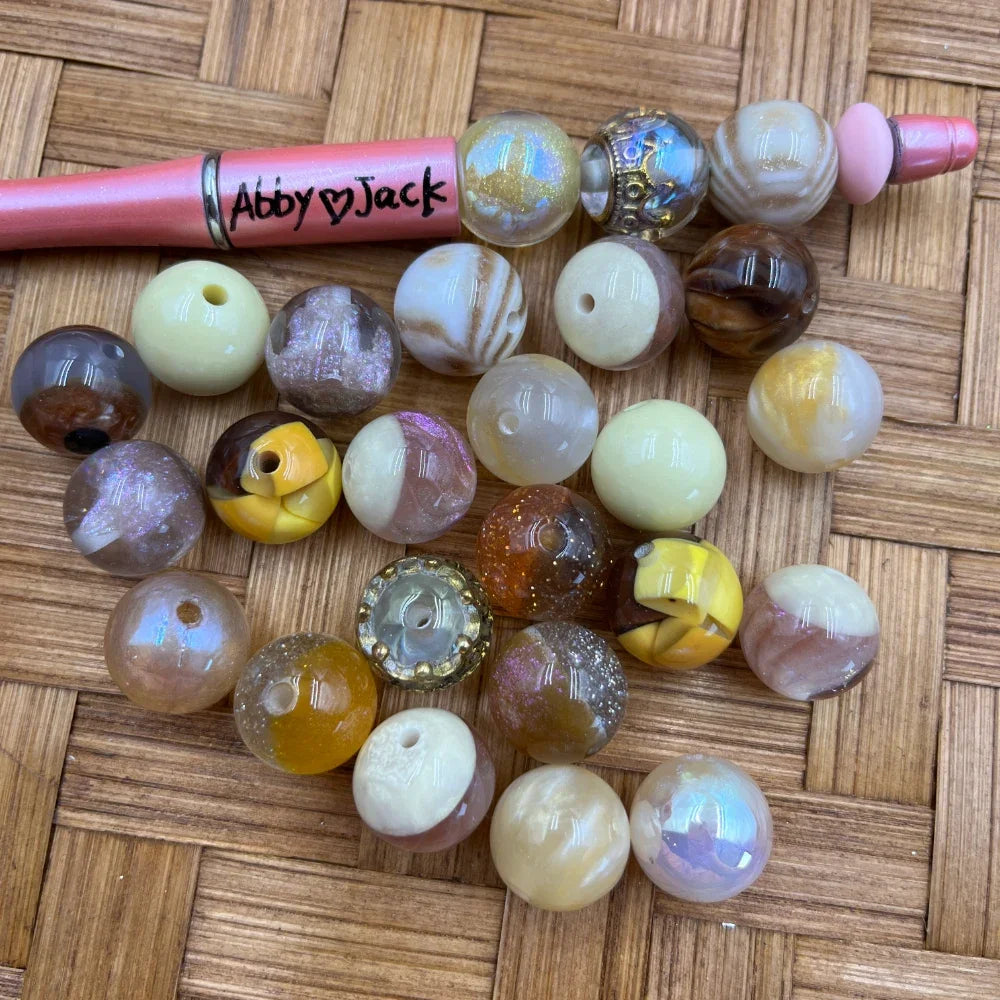 16MM neutral marble swirl iridescent acrylic beads in cream, brown, gold, and taupe tones displayed on a wicker surface next to a pink beadable pen labeled Abby and Jack.