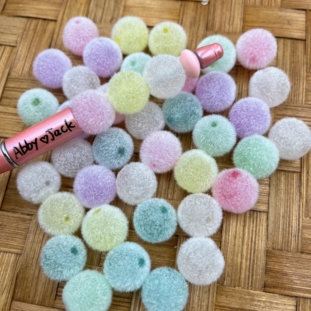 16MM pastel fuzzy velvet acrylic beads in assorted soft colors including pink, lavender, mint, yellow, and white, displayed on a wicker surface next to a beadable pen.