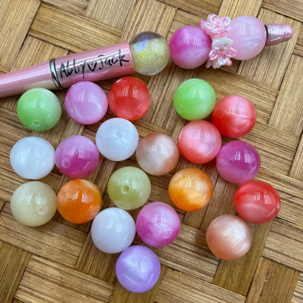 16MM pastel moonstone swirl acrylic beads in assorted colors including pink, green, orange, white, lavender, and coral, displayed next to a beadable pen on a wicker surface.