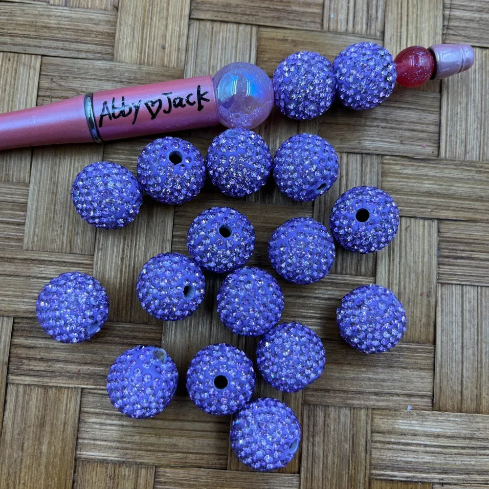 16MM purple clay rhinestone beads with sparkling crystal embellishments and drilled holes, displayed on a woven surface next to a beadable pen, ideal for DIY jewelry making and crafts.