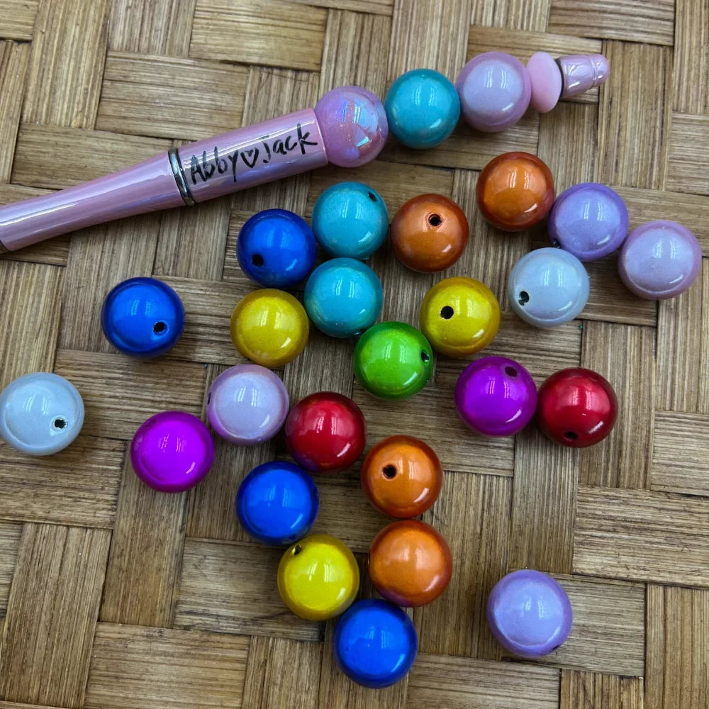 16MM rainbow miracle acrylic beads in assorted vibrant colors including blue, teal, yellow, green, red, orange, purple, and pink displayed on a woven surface next to a beadable pen.