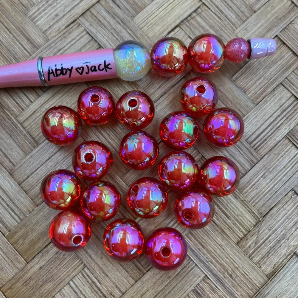 16MM red aurora AB iridescent acrylic beads with rainbow shimmer finish displayed on woven surface next to a beadable pen, showing hole detail for DIY jewelry making.