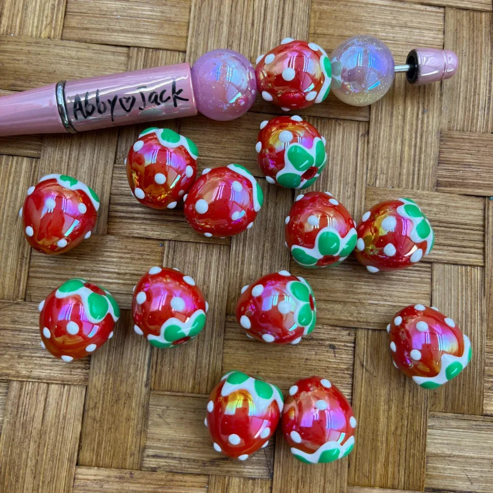 16MM red iridescent acrylic beads with white polka dots and green strawberry leaf pattern, shown with a pink beadable pen on a wicker surface.