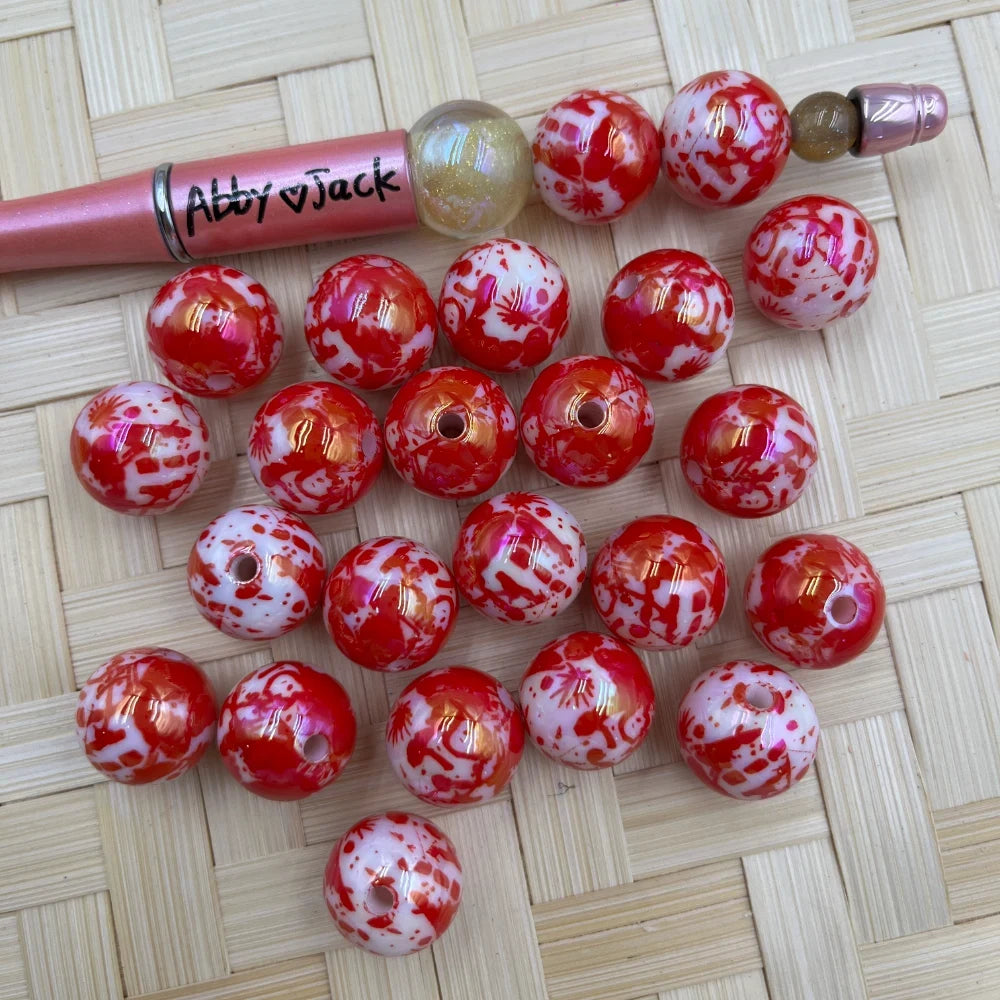 16MM red and white paint splatter AB finish acrylic beads with iridescent sheen, shown next to a beadable pen on a wicker surface, perfect for DIY jewelry making and beadable pens.