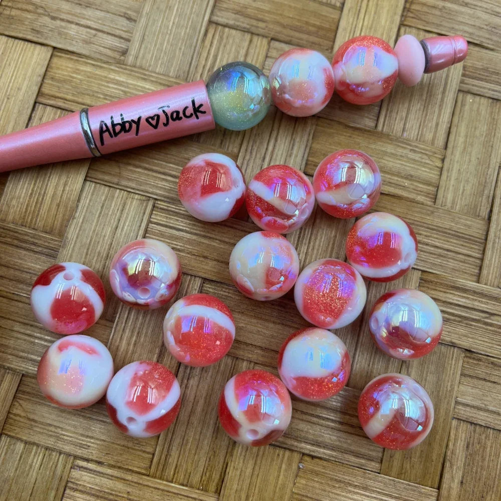 16MM red and white swirl iridescent acrylic beads with aurora shimmer finish displayed on woven surface next to a pink beadable pen