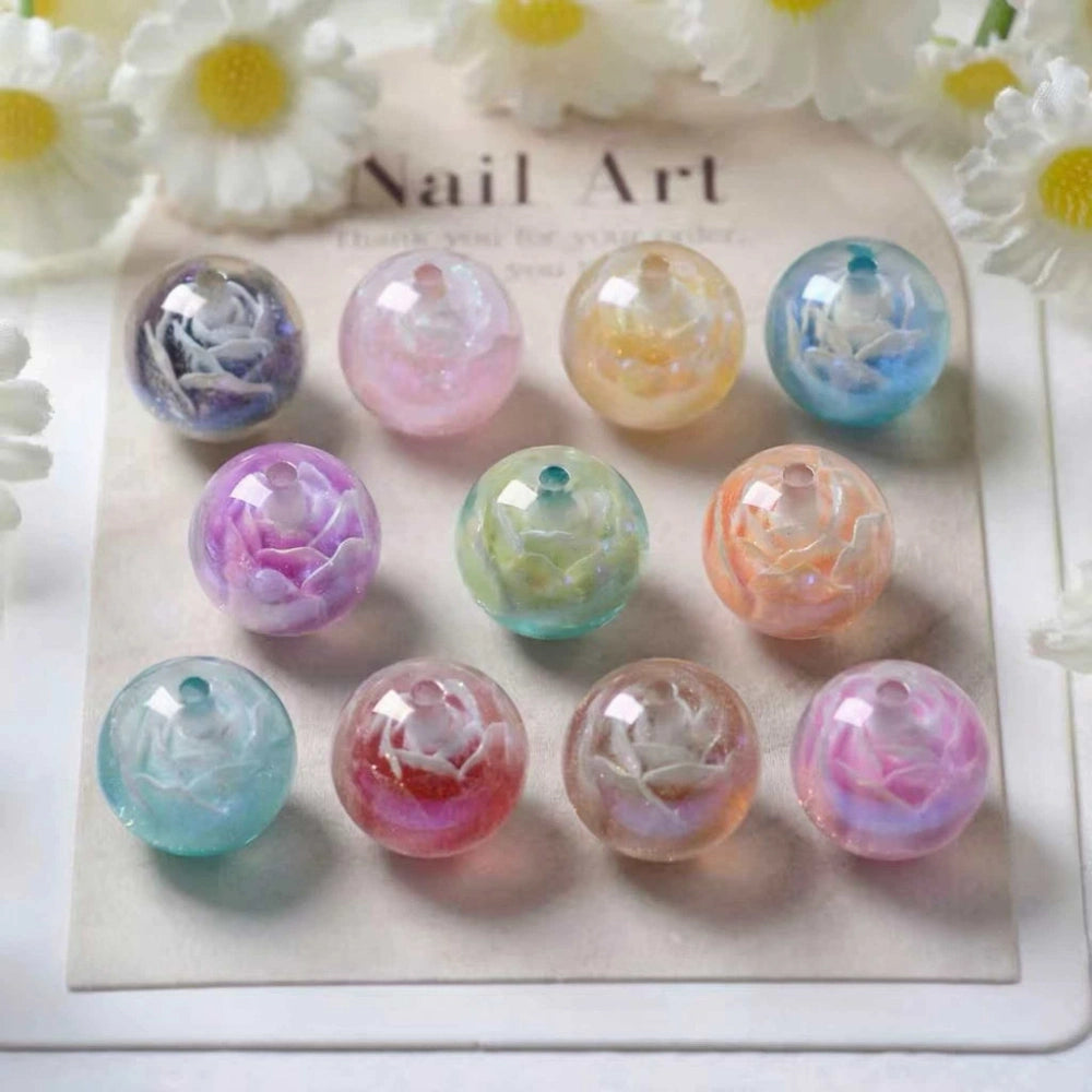 10 round iridescent acrylic beads with encased white rose flower design in assorted pastel aurora colors including purple, pink, teal, orange, and green displayed on a nail art card with white daisy flowers in background