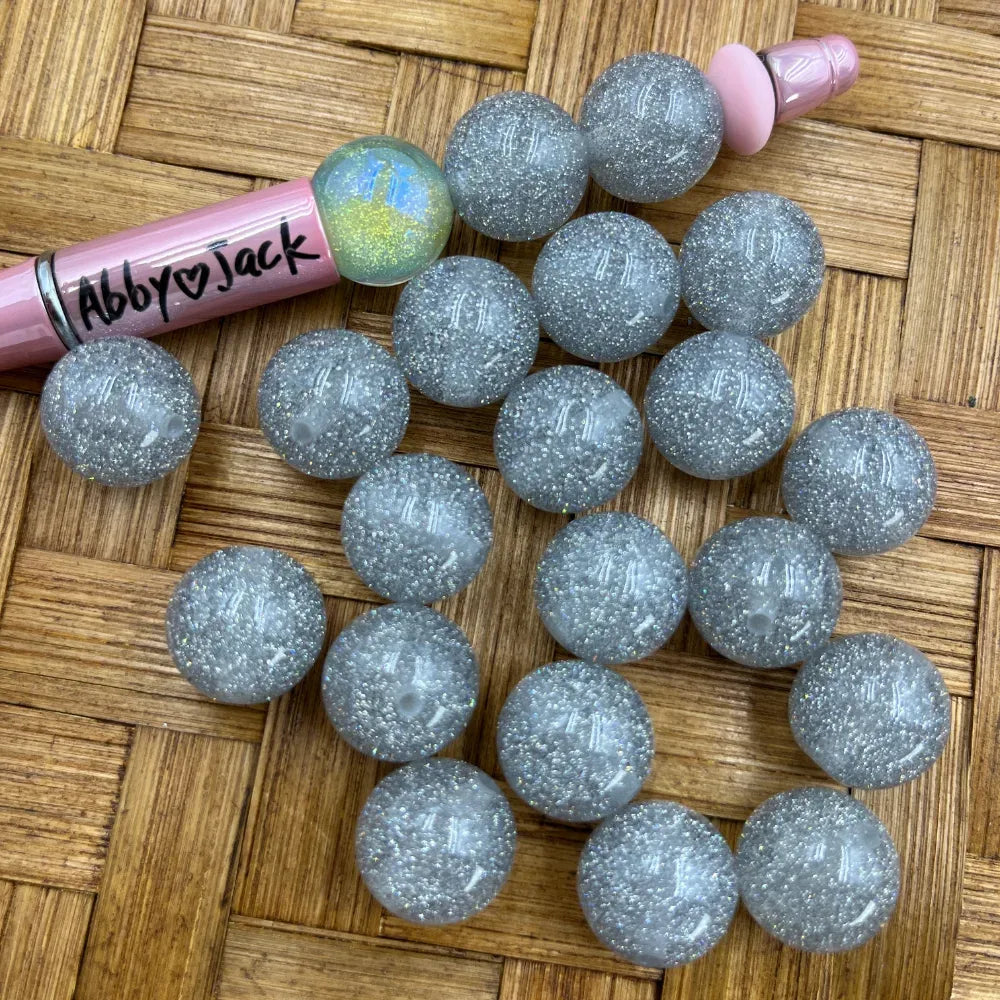16MM silver glitter acrylic beads with iridescent sparkle finish displayed next to a pink beadable pen on a wicker surface from DIY Mini Planet.