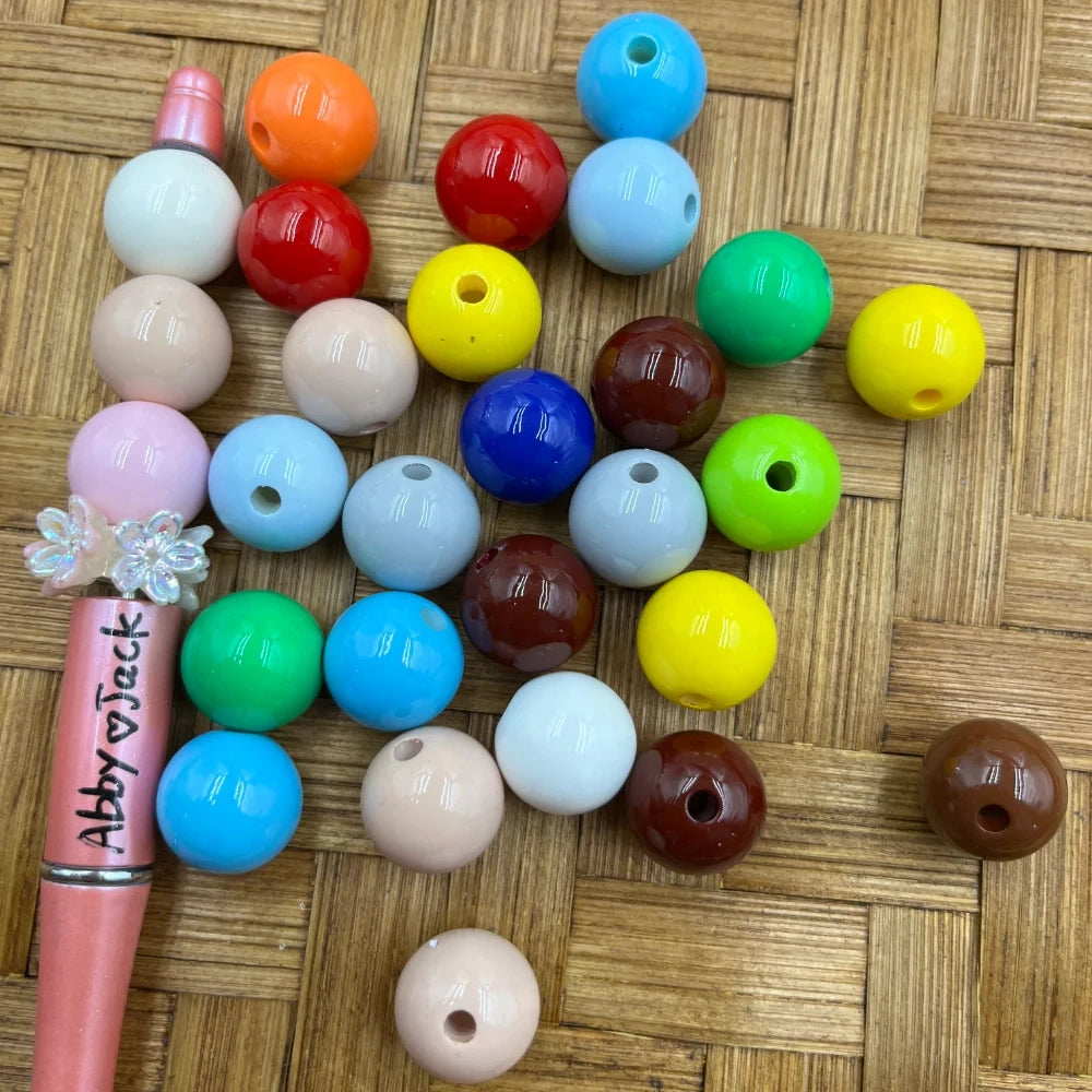 16MM solid color acrylic round beads in assorted colors including red, blue, yellow, green, brown, pink, white, and light blue arranged on a wicker surface next to a beadable pen.