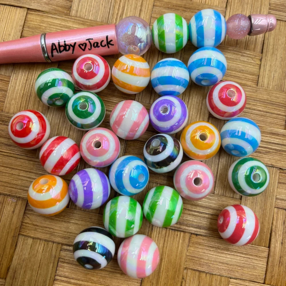 16MM multicolor striped acrylic beads in assorted colors including red, blue, green, pink, purple, orange, and black with white stripes, displayed on a woven surface next to a beadable pen labeled Abby Jack.