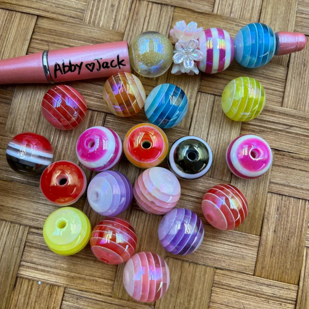 16MM multicolor striped swirl acrylic round beads in assorted colors including red, blue, yellow, pink, purple, and orange, shown next to a beadable pen on a wicker surface.