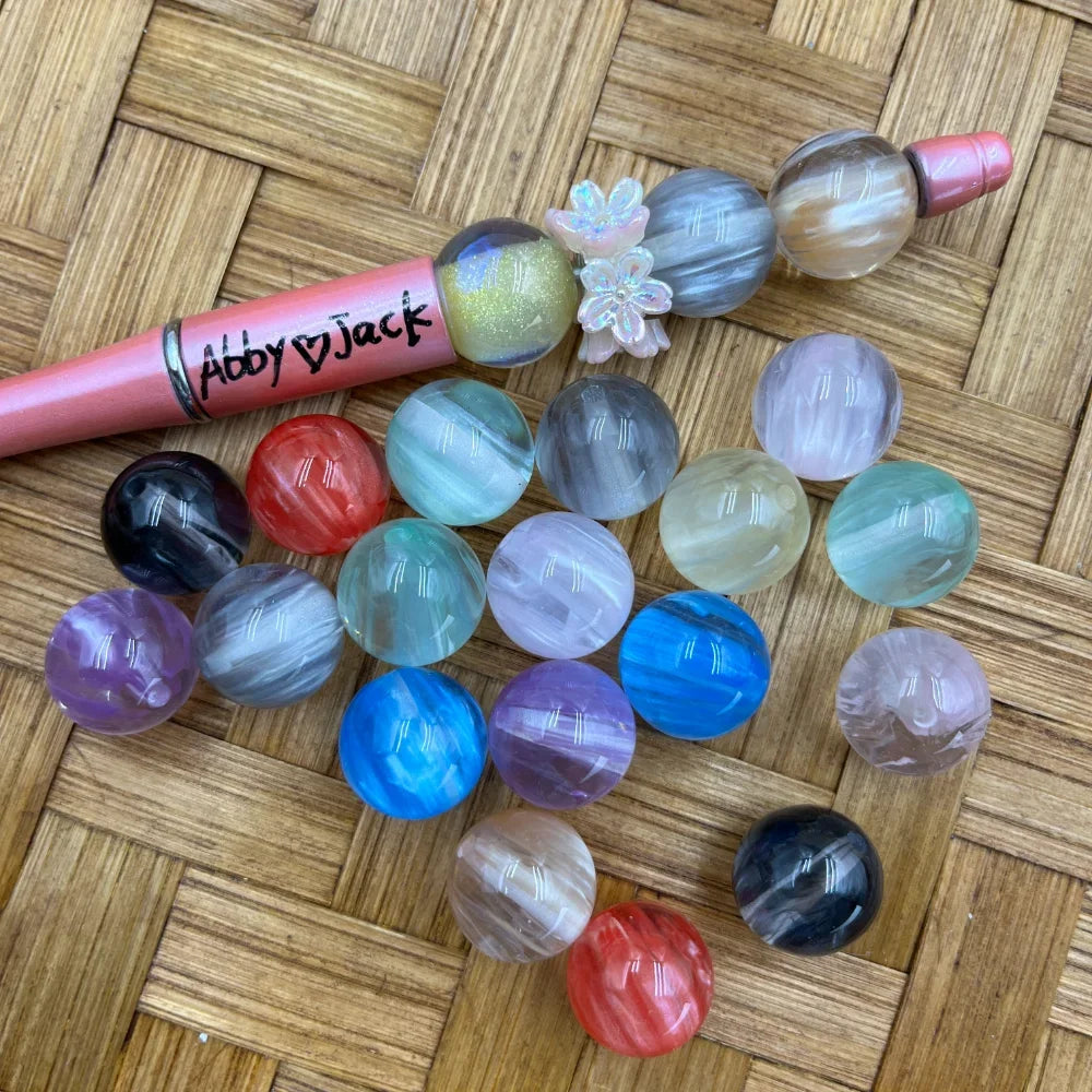 16MM swirl marble acrylic beads in assorted colors including blue, purple, red, black, gray, green, and pink displayed on a woven surface next to a beadable pen.