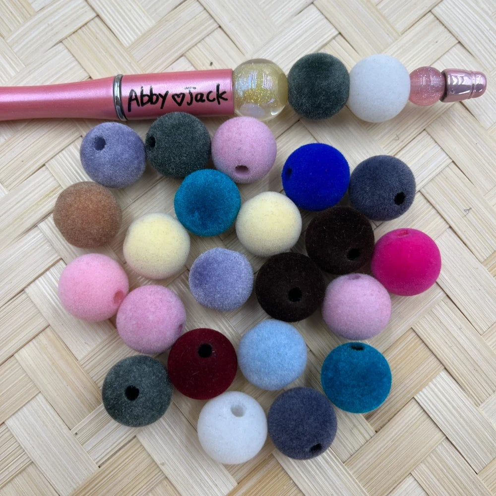 16MM velvet flocked acrylic beads in assorted colors including pink, blue, teal, gray, white, maroon, and more, displayed on a woven surface next to a beadable pen.