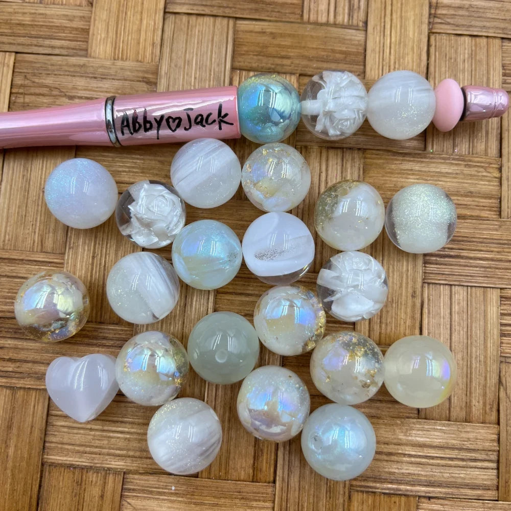 16MM white aurora iridescent acrylic beads with rose and opalescent shimmer designs displayed on wicker surface next to a pink beadable pen labeled Abby heart Jack