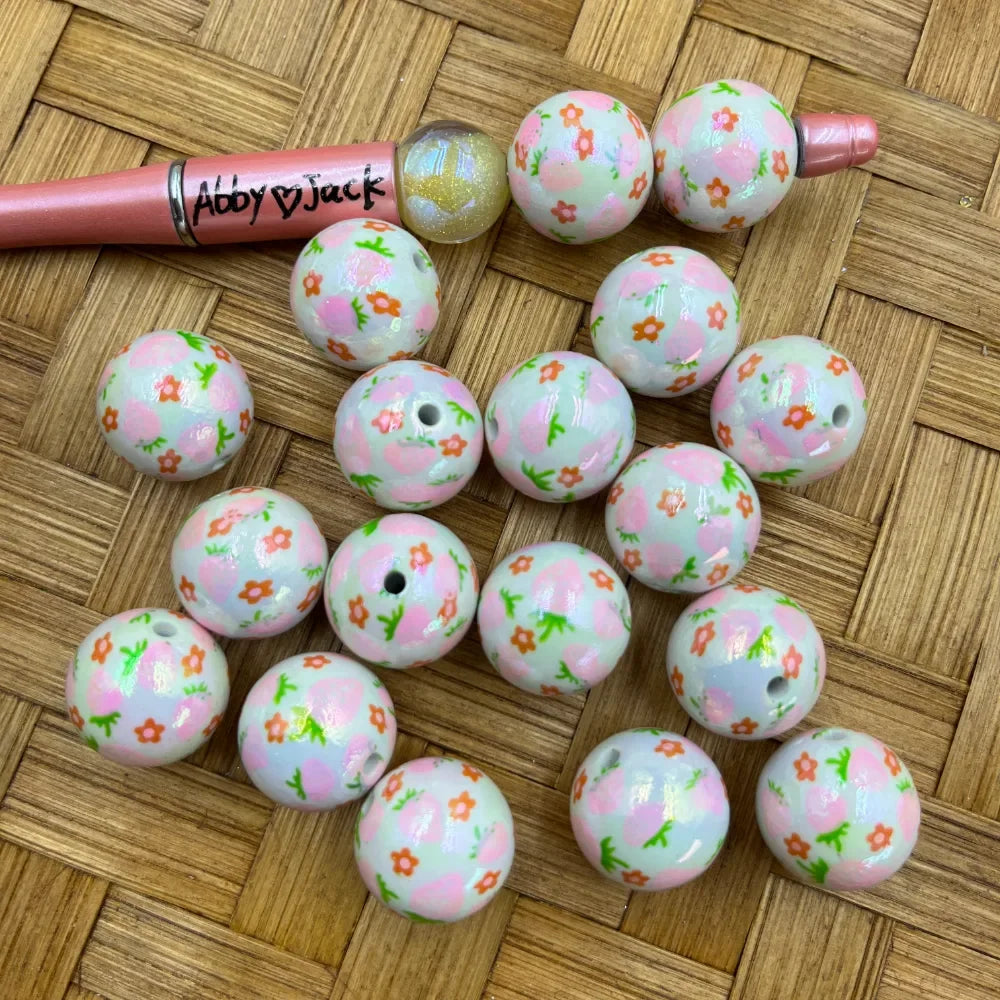 20MM white acrylic round beads with pink floral pattern, orange flowers, and green leaves, displayed on a woven surface next to a beadable pen.
